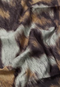 Textilie s vlnitým vzorem v hnědých, béžových a černých odstínech. Měkká textura s jemným leskem, vykazující vlastnosti přírodních vláken.