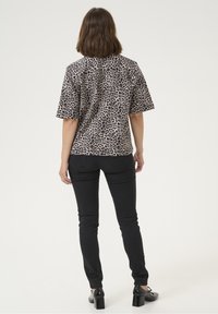 Camicia a maniche corte con stampa leopardata in taupe e nero, abbinata a jeans neri aderenti. La camicia presenta una vestibilità comoda e un design semplice.