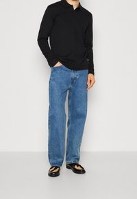 Czarna longsleeve polo, niebieskie luźne dżinsy i czarne buty z teksturalnym wzorem. Prosty, codzienny strój o swobodnym kroju.