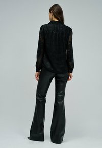 Czarna przezroczysta bluzka z kwiatowym wzorem, z długimi rękawami i okrągłym kołnierzykiem, zestawiona z rozszerzającymi się czarnymi spodniami skórzanymi.