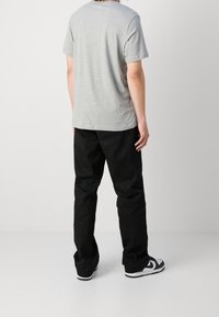 Šedé bavlněné tričko s krátkým rukávem, doplněné černými kalhotami; osoba otočená zády, oblečená v černo-bílých teniskách.