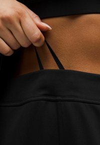 Juodas sportinis apranga su lygiu paviršiumi, turintis plonas petnešas, ištrauktas iš sportinės maikutės, pabrėžiantis elegantišką dizainą ir prigludimą.