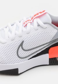 Hvide mesh Nike sneakers med grå accenter, en markant sort sål og en orange hældetalje; har et tekstureret mønster og flade snørebånd.