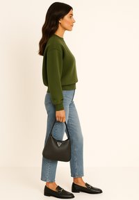 Groene cropped sweatshirt, lichtblauwe jeans, zwarte loafers en een kleine zwarte handtas met een logo-detail. Zijaanzicht van de outfit.