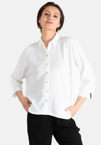 Camisa blanca de manga larga con botones y un corte relajado, hecha de una tela suave, con un cuello clásico y sutiles detalles de botones.