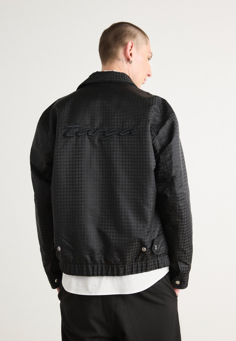 Veste bomber noire texturée avec un motif à carreaux, arborant un logo "Targa" brodé, des fermetures à pression et un ourlet élastiqué.