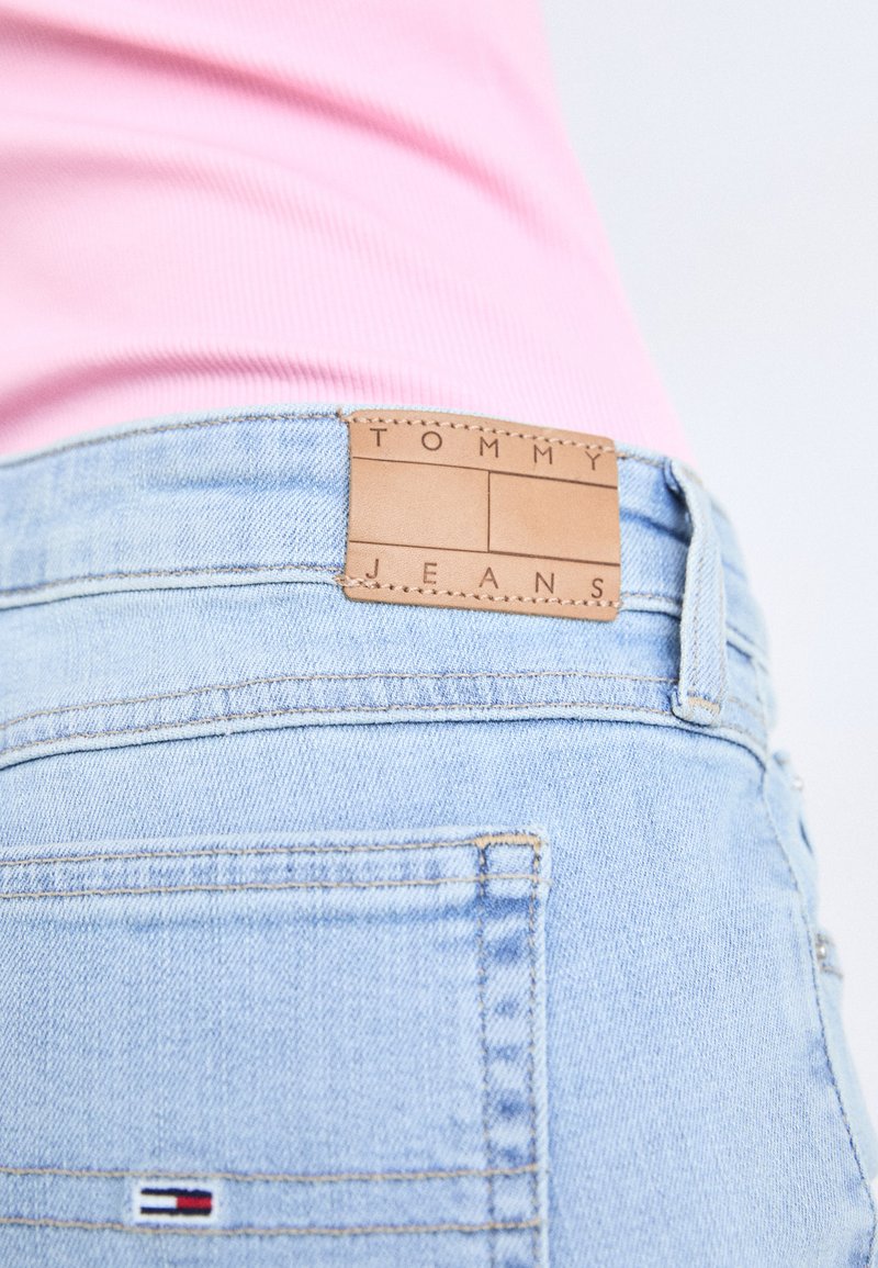 Hellblaue Denim-Jeans mit einem braunen Lederetikett auf dem Bund, das mit "TOMMY JEANS" beschriftet ist. Sie haben sichtbare Nähte und eine Gesäßtasche.
