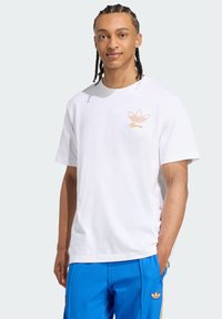 Witte katoenen t-shirt met korte mouwen en een ronde halslijn, voorzien van een oranje geborduurd logo op de linkerborst.