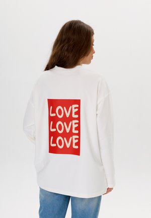 Biała, oversize'owa bluza z kapturem, z czerwonym prostokątem z powtarzającym się tekstem „LOVE” w kolorze kremowym. Miękka tkanina, luźny krój, długie rękawy.