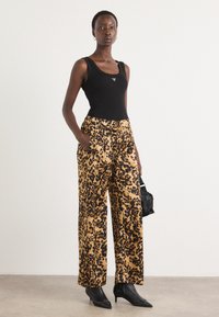 Top senza maniche nera abbinata a pantaloni larghi con stampa leopardata in tonalità dorate e nere. Indossato con tacchi neri a punta e una borsa piccola.