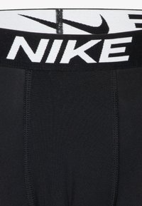Κοντινή λήψη μαύρης ζώνης εσώρουχου Nike με λευκό λογότυπο και το σύμβολο swoosh της Nike, ορατές ραφές στο μαύρο ύφασμα κάτω από το λάστιχο.