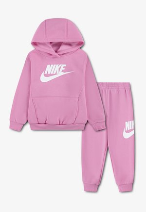 Różowa bluza z kapturem Nike i pasujące spodnie dresowe z białym logo Nike na przedzie i lewym udzie, przedstawione na jasnym tle.