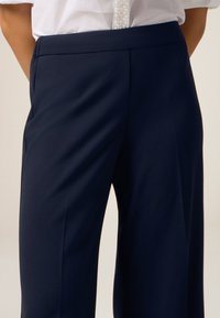 Navyblauwe wijdvallende broek met een gladde textuur, voorzien van een platte tailleband en voorplooien, ontworpen voor een getailleerde pasvorm.