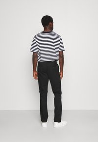 Pantalon noir associé à un T-shirt à manches courtes rayé noir et blanc. Le T-shirt a une coupe ample ; les chaussures sont blanches et épaisses.