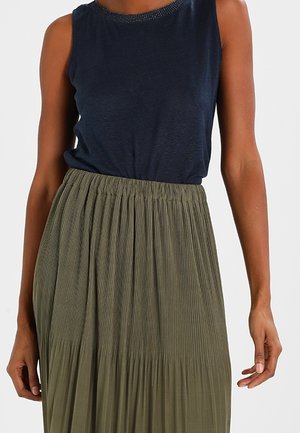 Sleeveless navy blue top tucked into high-waisted, olive green pleated skirt with gathered waistband on a standing person.