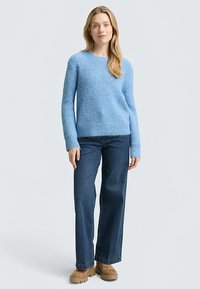 Világoskék, kötött pulóver kör alakú nyakkivágással és hosszú ujjakkal, sötétkék bő szárú farmerrel és világosbarna platform cipővel párosítva.