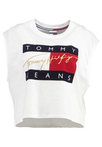 Bílý zkrácený tričko s výraznou grafikou v navy a červené barvě s nápisem "TOMMY" nad "JEANS" a zlatým podpisem na přední straně. Měkká látka.