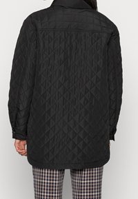 Black quilted jacket featuring a collar, long sleeves, and a relaxed fit. The fabric has a diamond pattern and smooth texture.