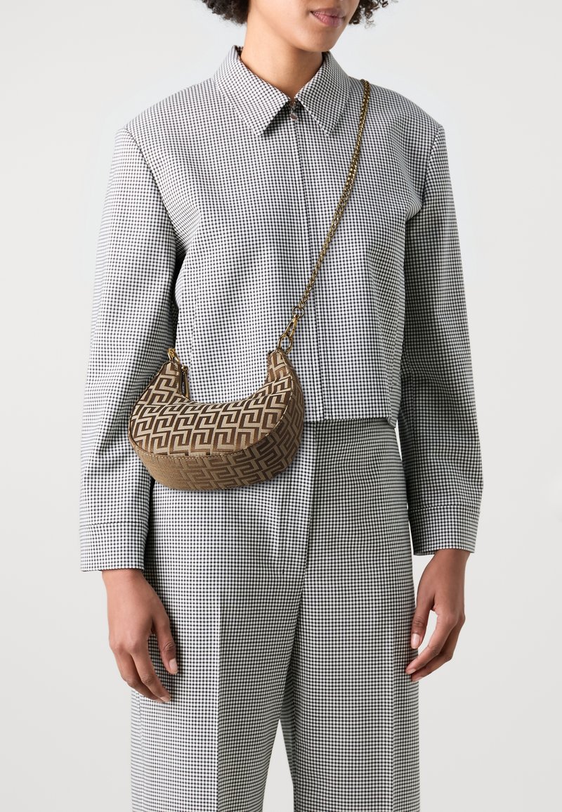 Femme portant un costume à carreaux noir et blanc avec un sac bandoulière en forme de croissant à motif marron et une sangle en chaîne dorée portée en travers de la poitrine.