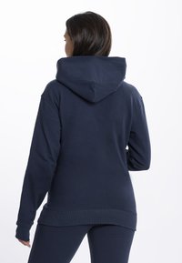 Kék kapucnis pulóver laza fazonnal, bordás mandzsettákkal és aljjal. Puha textúra minimalista kialakítással, látható logók vagy minták nélkül.