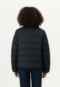 Zwarte pufferjack met een boxy pasvorm, horizontale stiksels, hoge kraag en aansluitende mouwen. Het materiaal lijkt glad en iets glanzend.