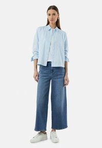 Lichtblauwe gestreepte overhemden met knopen, witte t-shirt eronder, gecombineerd met wijde blauwe jeans en witte sneakers. Eenvoudig en casual ontwerp.