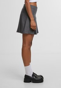 Harmaa laskostettu hame, jossa on levenevä muotoilu, valmistettu kevyestä kankaasta. Yhdistetty mustiin alustaloihinsa ja valkoisiin nilkkasukkiin.