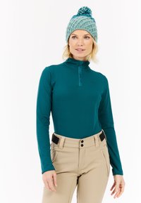 Tyrkysový dlouhý rukáv s polo zipem, spárovaný se béžovými kalhotami se dvěma bočními kapsami a páskem. Pletená světle modrá čepice s bambulí.