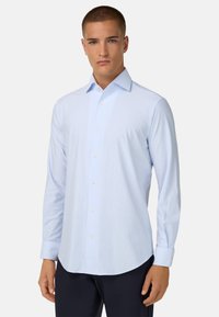 Lichtblauw button-up shirt van stof met verticale witte strepen. Heeft een puntige kraag en lange mouwen met knoopmanchetten.