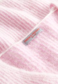 Różowy sweter w paski wykonany z miękkiego materiału. Posiada naszytą metkę z marką "FRIEDA & FREDDIES" oraz instrukcje dotyczące pielęgnacji.