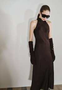 Vestido negro de cuello halter con una silueta elegante, hecho de una tela suave, combinado con guantes largos oscuros y gafas de sol negras de gran tamaño.