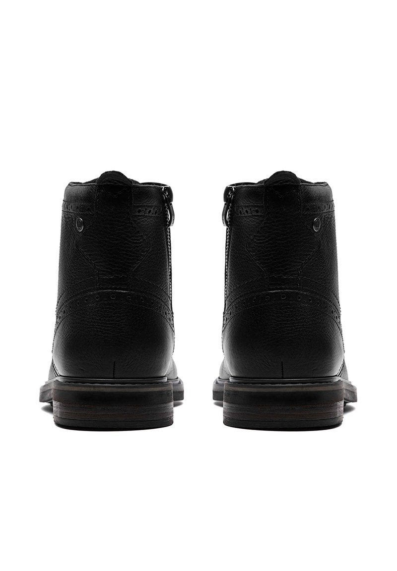 Stivaletti neri in pelle con una texture liscia, dettagli brogue e un tacco in legno basso. Presentano una zip laterale per una facile vestibilità.