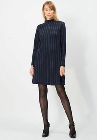 Marineblå kjole med lodrette hvide striber, falsk turtleneck og lange ærmer. A-formet snit, over knæ længde. Sammen med sorte hæle og strømpebukser.