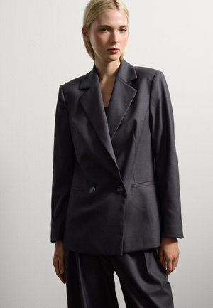 Blazer double boutonnage gris foncé avec des revers crantés, deux boutons et poches avant. Fait en tissu lisse avec des épaules structurées.