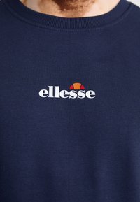 Sudadera azul marino de algodón, con un logo blanco de "ellesse" y un gráfico multicolor (naranja y rojo) encima del texto.