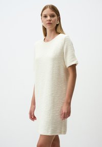 Abito a maniche corte in tessuto crema testurizzato, caratterizzato da un colletto rotondo e una silhouette dritta, che offre una vestibilità casual e rilassata.