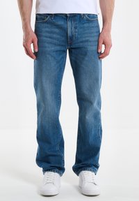 Jeans de mezclilla azul con un diseño de pierna recta, que presentan un estilo clásico de cinco bolsillos y un ligero desgaste. Combinados con zapatillas deportivas blancas.