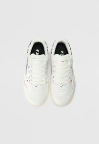 Białe sportowe sneakersy z teksturowaną powierzchnią, klasycznym zapięciem na sznurówki, wyściełanym kołnierzem oraz markowymi akcentami w czerni i czerwieni.