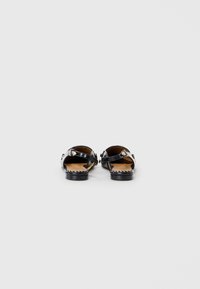 Black sandals with wide straps and silver hardware, featuring a flat sole and a smooth leather texture, viewed from the back.