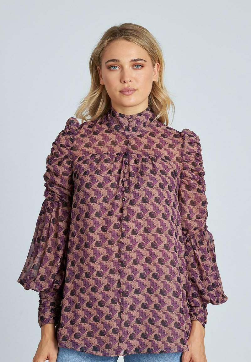 Blusa de manga larga y cuello alto en tejido transparente con un patrón floral en púrpura y negro, con botones en la parte delantera y mangas abullonadas.