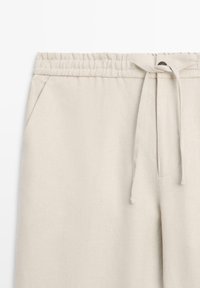 Beige linnenmix broek met elastische tailleband, voorzakken en een stoffen trekkoord dat in een strik aan de voorkant is gebonden.