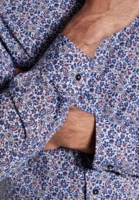 Blommönstrad skjorta i blått, rött och krämfärgat; har knappark and en klassisk kragdesign. Materialet verkar lätt och strukturerat.