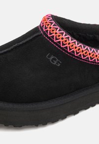 Svart mocka slip-on sko med en texturerad svart sula, med rosa och orange geometrisk broderi runt kragen och UGG-logotypdetalj.