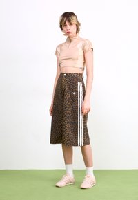 Beige, rövid ujjú cropped top, amelyet egy barna leopárdmintás szoknyával párosítottak, fehér oldalsávokkal és gombos záródással. A kinézetet edzőcipők teszik teljessé.