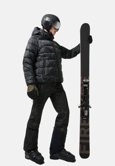 Schwarze Pufferjacke mit geometrischem Muster, schwarze Skihosen, Handschuhe und ein Snowboard mit Bindungen, getragen von einem Snowboarder in Ausrüstung.