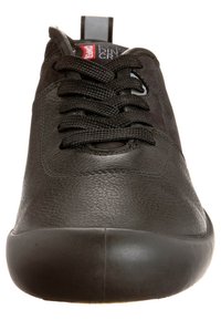 Sneaker en cuir noir avec surface texturée, bout arrondi, semelle épaisse et lacets noirs noués en un motif croisé standard.