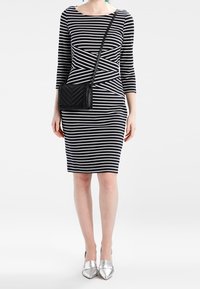 Schwarzes und weißes gestreiftes knielanges Kleid mit taillierter Form, Rundhalsausschnitt und dreiviertellangen Ärmeln, kombiniert mit einer schwarzen Umhängetasche.