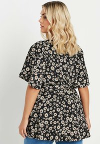 Top avvolgente nero con fiori bianchi e centri arancioni, maniche corte e vita aderente, realizzato in tessuto leggero.