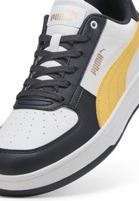 Puma sneakers med hvid læder, grå detaljer og et gult stribe. Har rund tå, perforeret overdel og flade snørebånd.