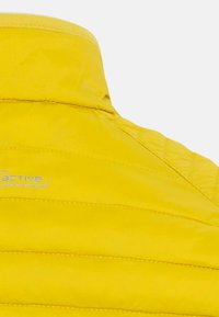 Gul pufferjakke med standkrave, præget af vertikal quilted struktur og et subtilt logo i lysegrå på stoffet.